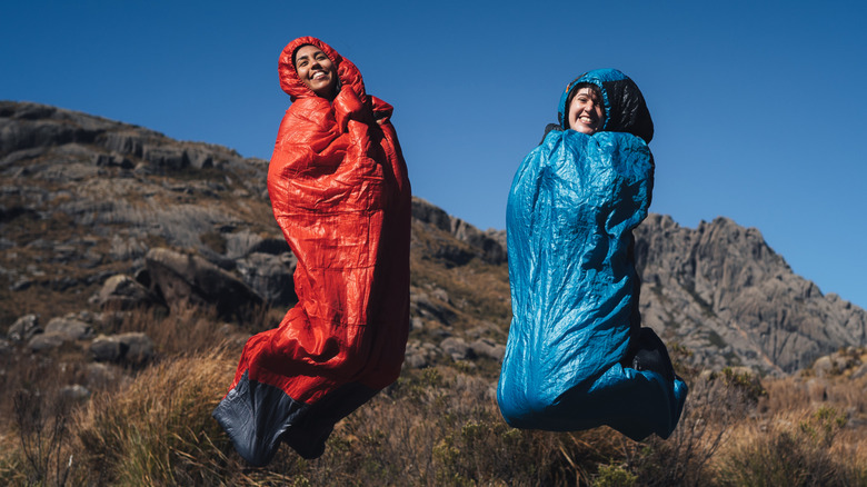 two people jumping inside sleeping bags in the mountains