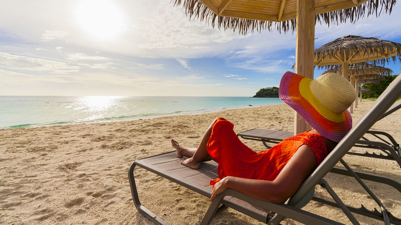 woman with red dress and hat resting on a chair at the beach